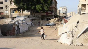Un niño pequeño lucha bajo el peso de un bidón de agua para llevarlo a la tienda de campaña de su familia desplazada.