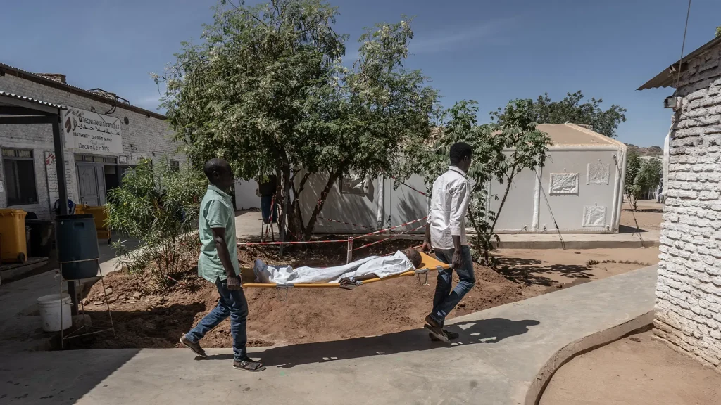 Dos trabajadores médicos de MSF transportan a un niño pequeño en una camilla desde el quirófano hasta la unidad de cuidados intensivos del Hospital París gestionado por MSF en Tawila.