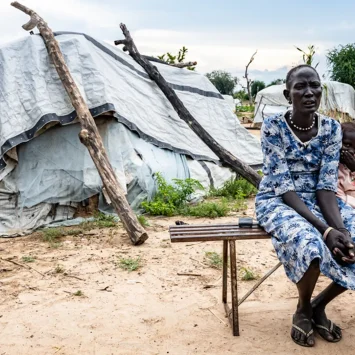 Arual Manyok y su hija Adit Ayuel se sientan en un banco frente a su refugio en un campamento de desplazados. Sudán del Sur, octubre de 2024.
