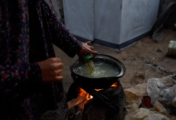 Una madre prepara comida para sus hijos y familia, vertiendo una lata de judías verdes en agua hirviendo sobre un fuego que ella misma enciende. La cantidad de ayuda humanitaria que entra en Gaza alcanza su nivel más bajo en meses.