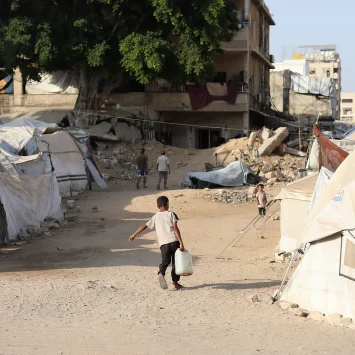 Un niño pequeño lucha bajo el peso de un bidón de agua para llevarlo a la tienda de campaña de su familia desplazada.