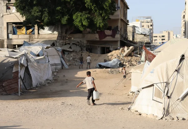 Un niño pequeño lucha bajo el peso de un bidón de agua para llevarlo a la tienda de campaña de su familia desplazada.