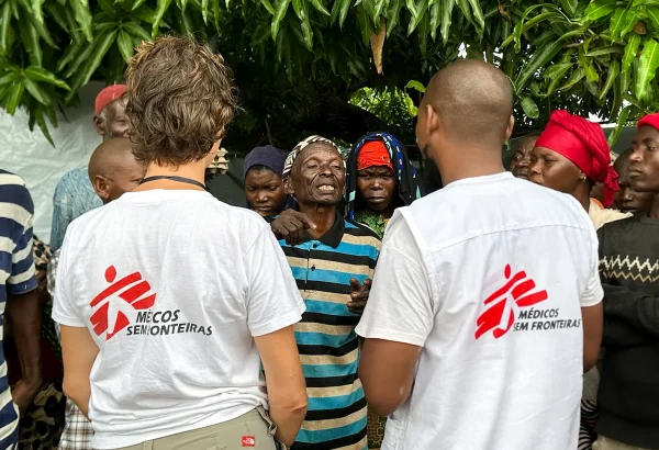 El personal de MSF Nathalie Gielen y Gimo Lazimo hablan con un grupo de personas desplazadas que esperan fuera de una clínica móvil de MSF en Alua Velha, distrito de Eráti, provincia de Nampula.