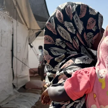 Amina* abraza a un niño frente a un refugio improvisado en Tawila. Mientras huía de El Fasher con sus hijos, fue violada por hombres armados. Estado de Darfur del Norte, Sudán, febrero de 2026. *Se ha utilizado un seudónimo para proteger su identidad.